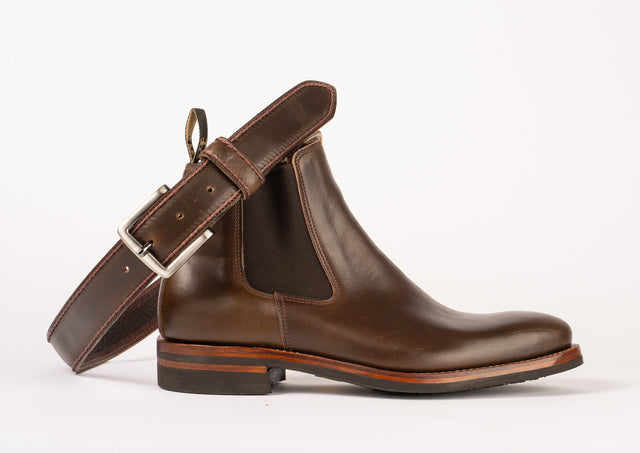 A brown leather belt with chain stitching, displayed alongside a Chelsea boot